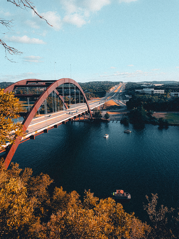 Pennybacker Bridge spanning Lake Austin, with boats on the water and tree-covered hills beyond