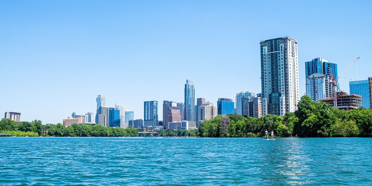 Austin skyline viewed across Lady Bird Lake, with paddleboarders near the tree-lined shore.