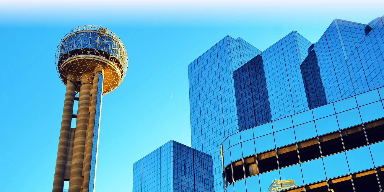 Reunion Tower beside reflective glass skyscrapers against a bright blue Dallas sky.