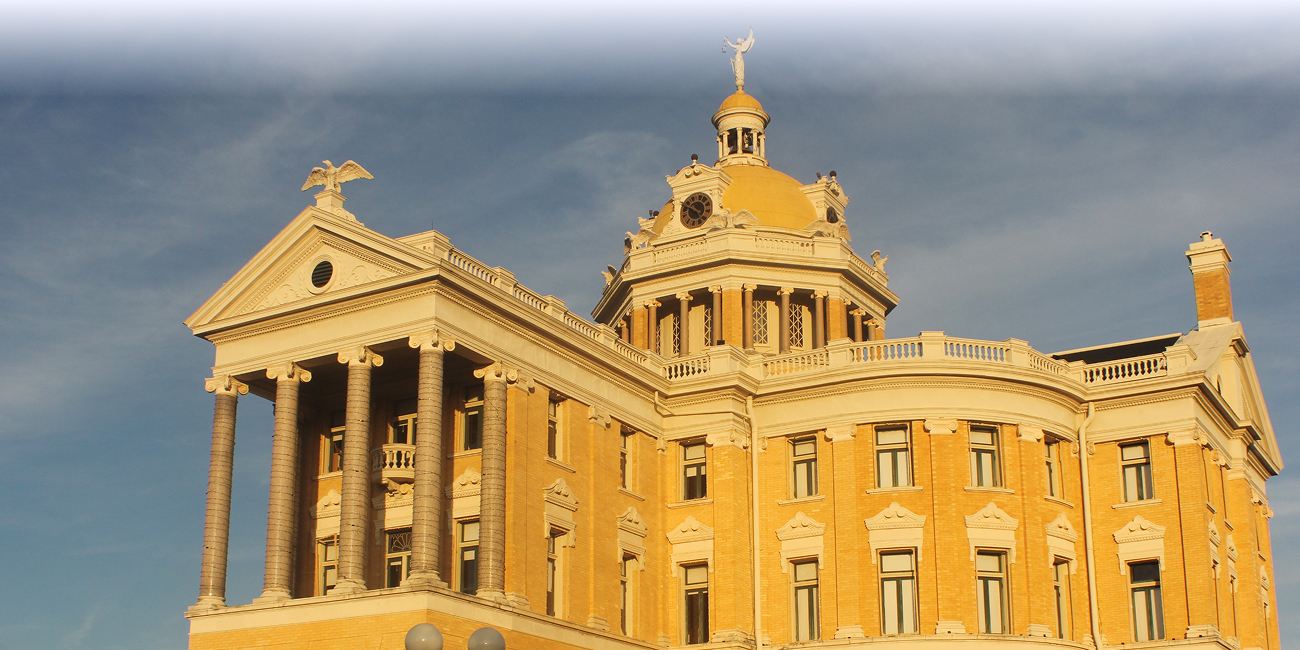 Historic domed courthouse with columns illuminated by warm sunlight beneath dark clouds.