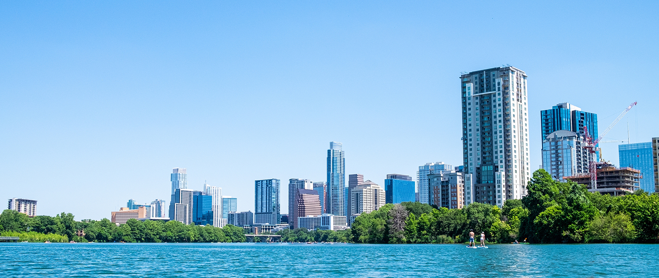 Austin skyline viewed across Lady Bird Lake, with paddleboarders near the tree-lined shore.