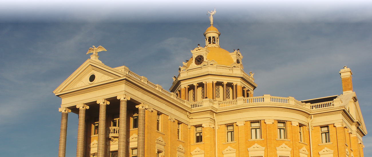 Historic domed courthouse with columns illuminated by warm sunlight beneath dark clouds.